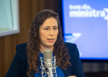 Mulher de cabelo cacheado fala ao microfone em estúdio com fundo desfocado