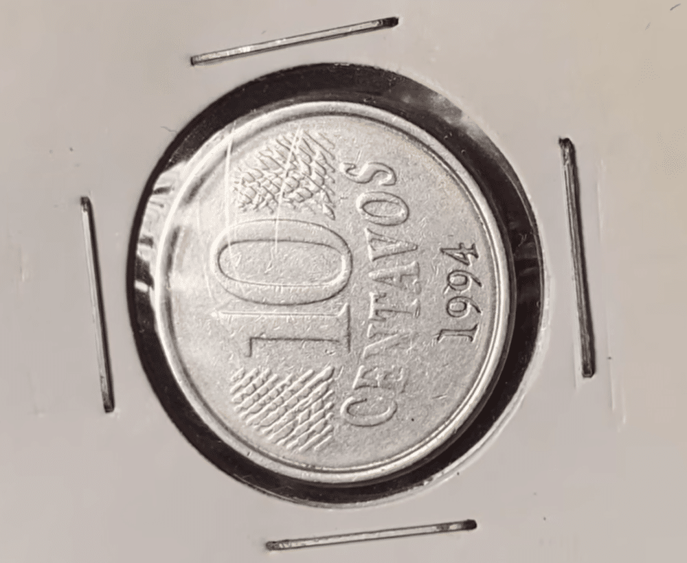 Moeda de 10 centavos de 1994 posicionada de lado dentro de um suporte de proteção, demonstrando o erro de cunhagem reverso horizontal para a esquerda.