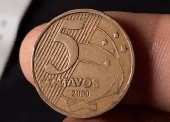 Close do reverso de uma moeda de 5 centavos do ano 2000, de cor bronze, sendo segurada por dedos. O foco está nos detalhes do cunho e na data.