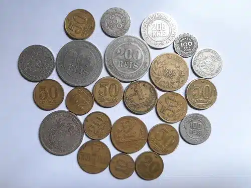 Coleção mista de moedas brasileiras antigas de Réis e Cruzeiros espalhadas sobre fundo branco, incluindo valores de 100, 200, 400 e 1000 Réis.