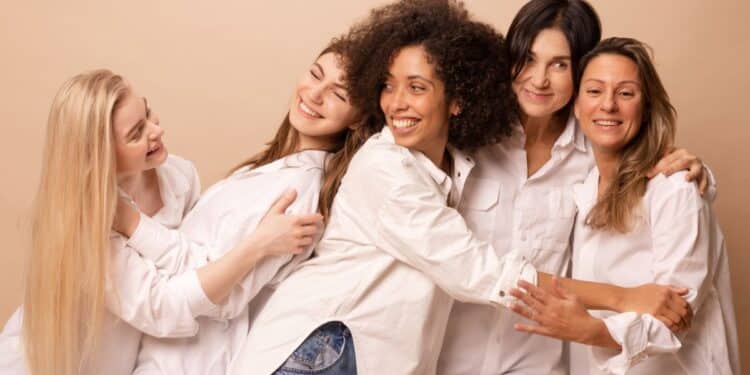 Cinco mulheres sorrindo e abraçadas representam união, diversidade e fortalecimento feminino na data de 8 de março.