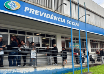 Grupo de pessoas em fila na entrada de agência da Previdência Social em dia nublado