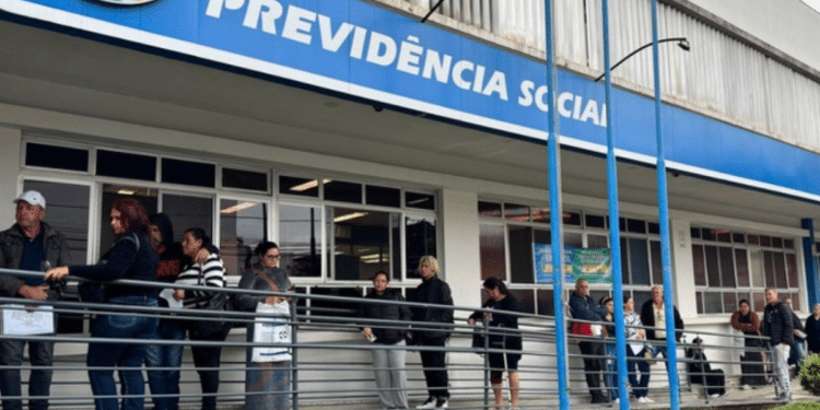 Grupo de pessoas em fila na entrada de agência da Previdência Social em dia nublado