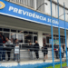 Grupo de pessoas em fila na entrada de agência da Previdência Social em dia nublado