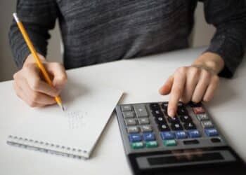 Pessoa usando calculadora e anotando valores para organizar dívidas e aproveitar programa de renegociação bancária.