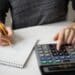 Pessoa usando calculadora e anotando valores para organizar dívidas e aproveitar programa de renegociação bancária.