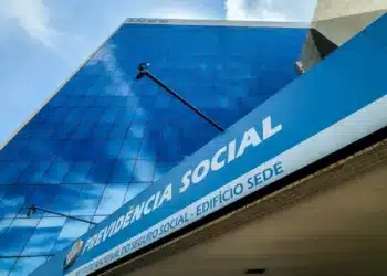 Edifício sede do INSS, com fachada espelhada refletindo o céu e com o nome 'Previdência Social' em destaque.