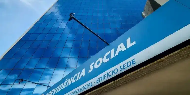 Edifício sede do INSS, com fachada espelhada refletindo o céu e com o nome 'Previdência Social' em destaque.