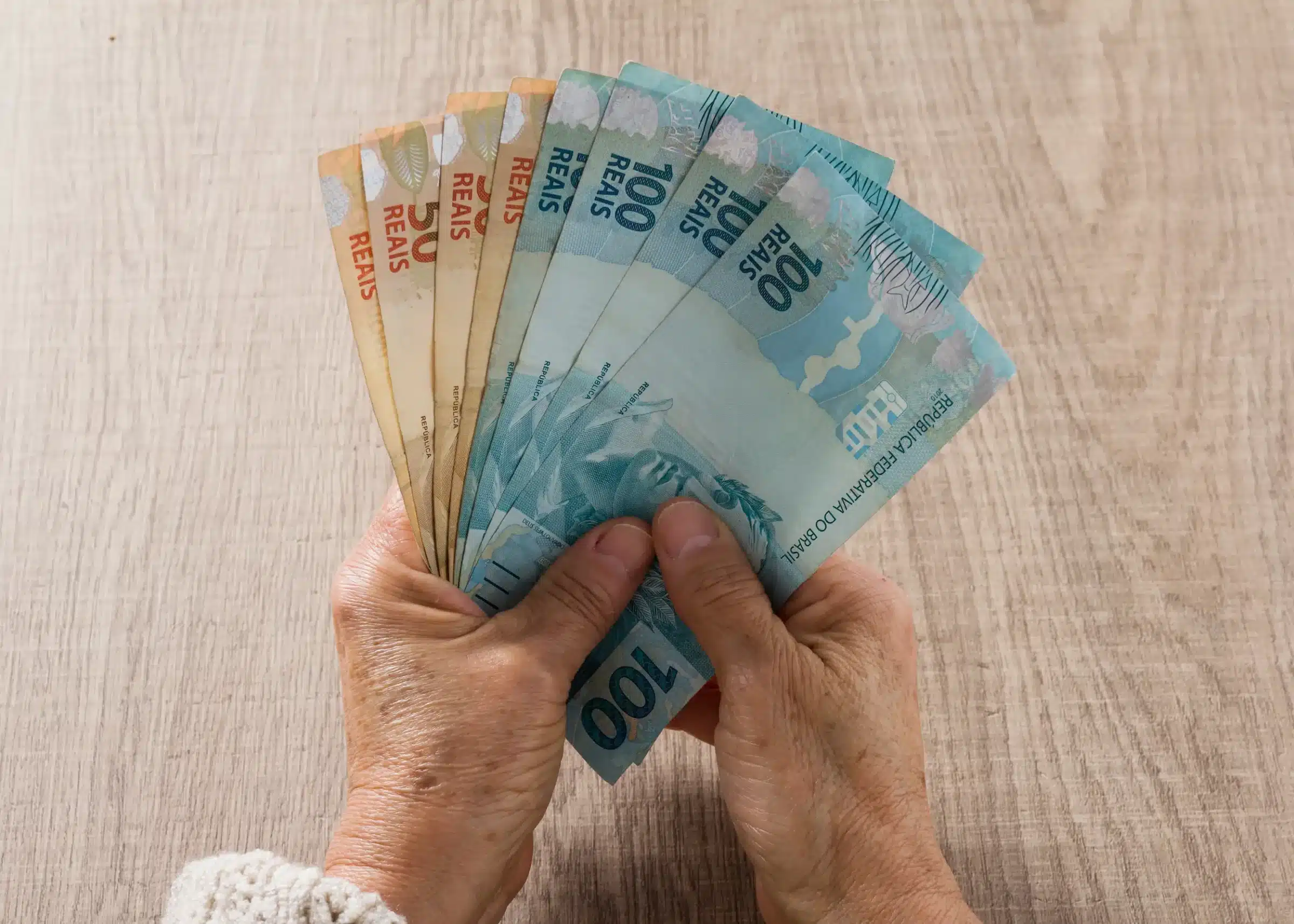 Cédulas de real nas mãos de um beneficiário representando as datas de pagamento da primeira parcela do décimo terceiro do INSS.