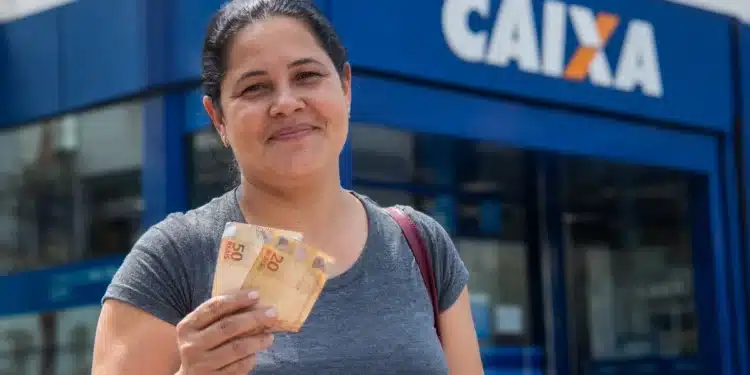 Beneficiária segura cédulas em frente a uma agência da Caixa, representando o pagamento do Bolsa Família de julho, que pode chegar a R$ 1.000, para beneficiários com NIS final 2.