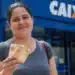Beneficiária segura cédulas em frente a uma agência da Caixa, representando o pagamento do Bolsa Família de julho, que pode chegar a R$ 1.000, para beneficiários com NIS final 2.