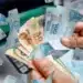 Pessoa segurando notas de real brasileiras com cédulas de 50 e 100 reais representando pagamentos do INSS de até R$ 8.475,55