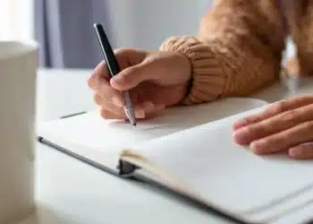 Pessoa escrevendo em um caderno durante estudo sobre palavras da língua portuguesa que não possuem forma no plural