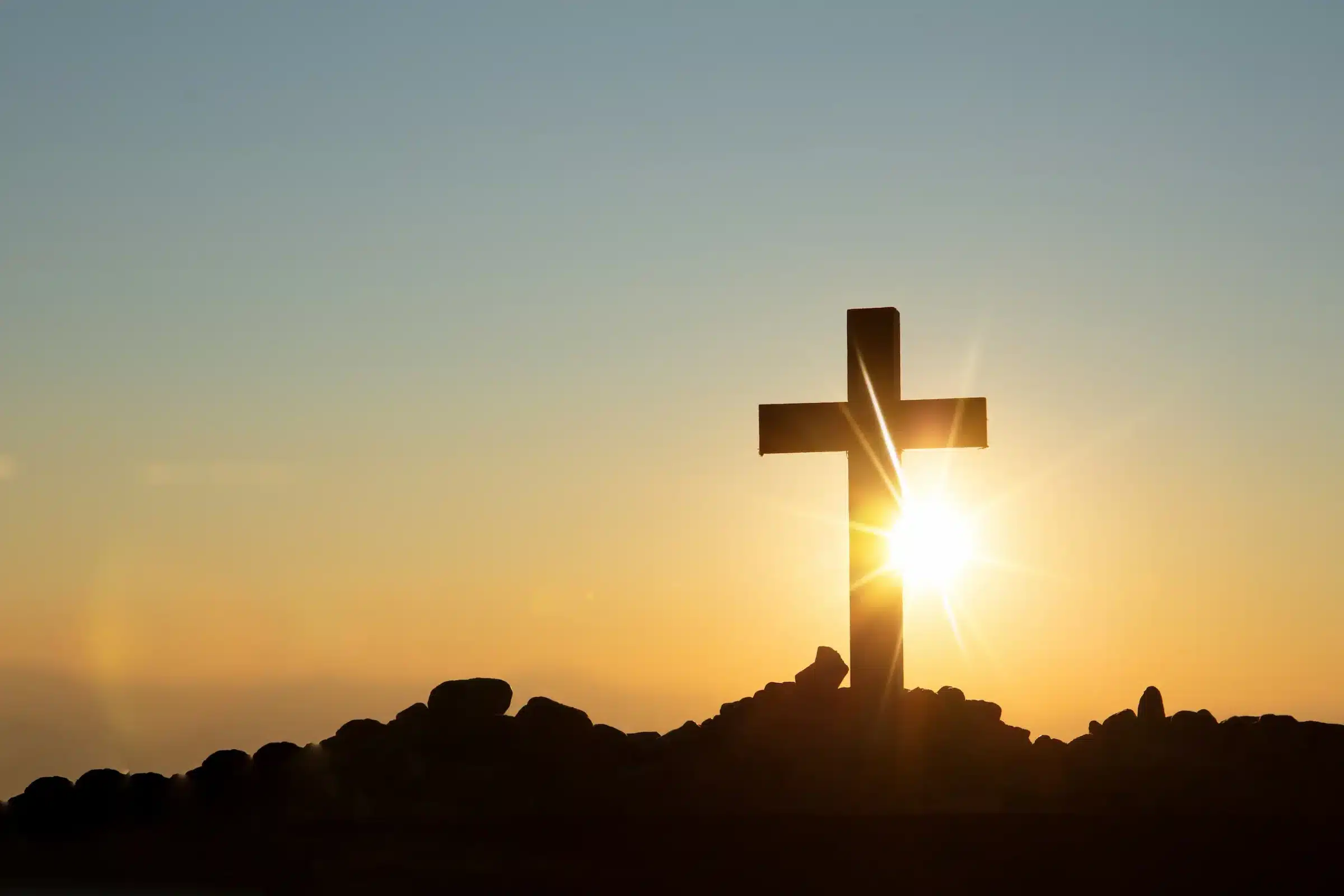 Cruz cristã iluminada pelo nascer do sol simbolizando a ressurreição de Cristo na celebração da Páscoa.