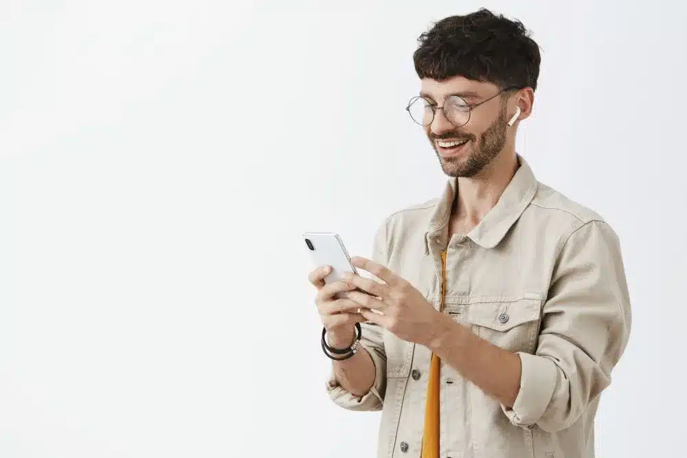 Homem sorridente usando fones de ouvido, olhando para o celular, em fundo branco, representando o passo a passo para apostar na Dupla de Páscoa.
