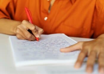 Mãos escrevendo em caderno com caneta vermelha representando processo seletivo da Prefeitura com salários de até R$ 3,8 mil