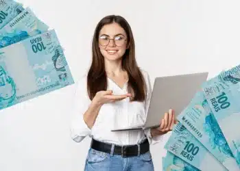 Mulher sorridente usando notebook, rodeada por notas de 100 reais, fundo branco