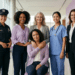 Seis mulheres diversas em trajes profissionais posam sorrindo em ambiente corporativo moderno