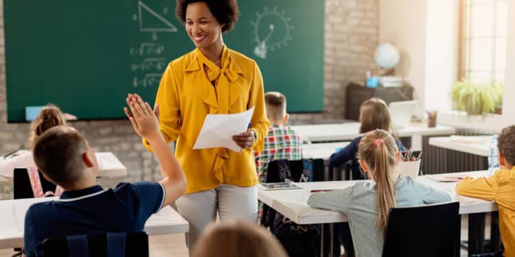 Professora sorrindo em sala de aula com alunos levantando a mão — proposta de novos adicionais salariais para professores 2026