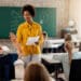 Professora sorrindo em sala de aula com alunos levantando a mão — proposta de novos adicionais salariais para professores 2026