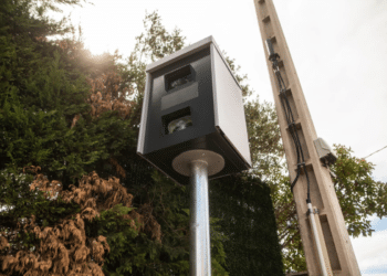 Radar fixo em poste monitora tráfego com árvores e céu claro ao fundo