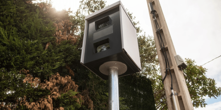 Radar fixo em poste monitora tráfego com árvores e céu claro ao fundo