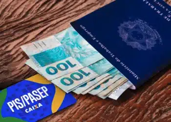 Cédulas de R$100 saindo de um passaporte brasileiro ao lado de cartão PIS/Pasep, ilustrando pagamento do PIS/Pasep liberado em 25/03.