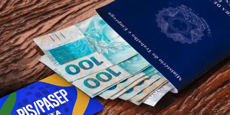 Cédulas de R$100 saindo de um passaporte brasileiro ao lado de cartão PIS/Pasep, ilustrando pagamento do PIS/Pasep liberado em 25/03.