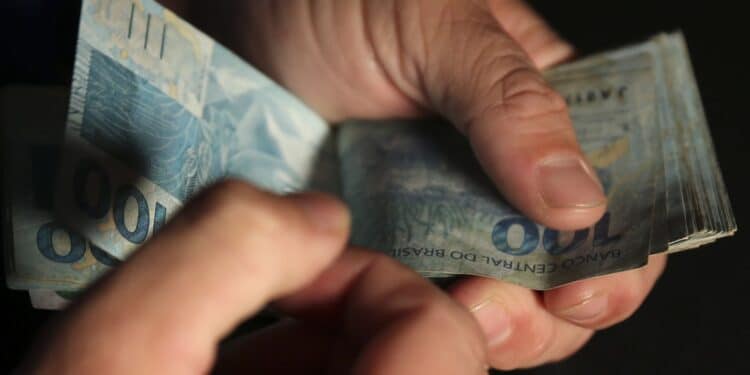 Mãos contando notas de reais — saque calamidade FGTS Caixa R$ 6.220 abril 2026
