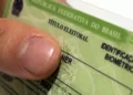 Close de um título de eleitor brasileiro com identificação biométrica sendo segurado por uma pessoa, representando o prazo para emissão do primeiro documento eleitoral.
