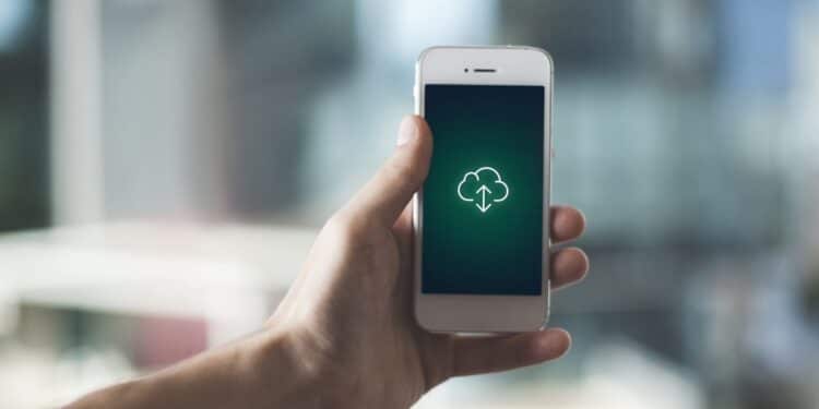 Pessoa segurando um iPhone com o ícone de nuvem na tela, representando a transferência de dados para outro dispositivo.