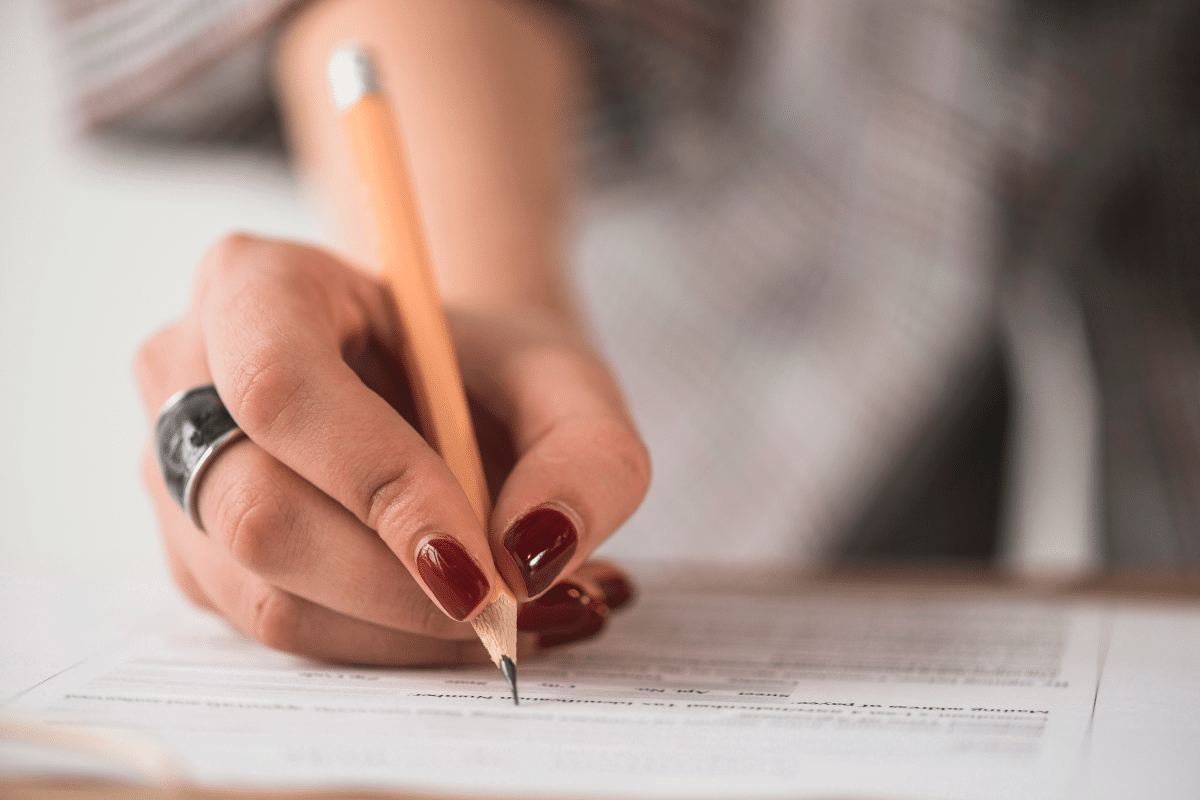 Mão com unhas vermelhas escreve respostas em folha de prova com lápis