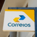 Placa dos Correios com logotipo amarelo e azul fixada na fachada de prédio