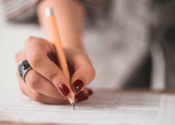 Mão feminina segurando lápis escreve respostas em folha de prova