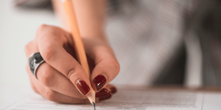 Mão feminina segurando lápis escreve respostas em folha de prova