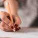 Mão feminina segurando lápis escreve respostas em folha de prova