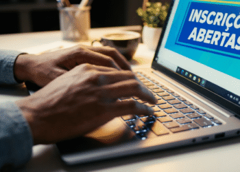 Pessoa digitando no notebook com tela mostrando aviso de inscrições abertas