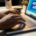 Pessoa digitando no notebook com tela mostrando aviso de inscrições abertas