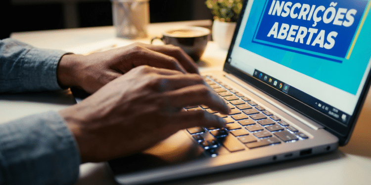 Pessoa digitando em notebook com tela exibindo aviso de inscrições abertas