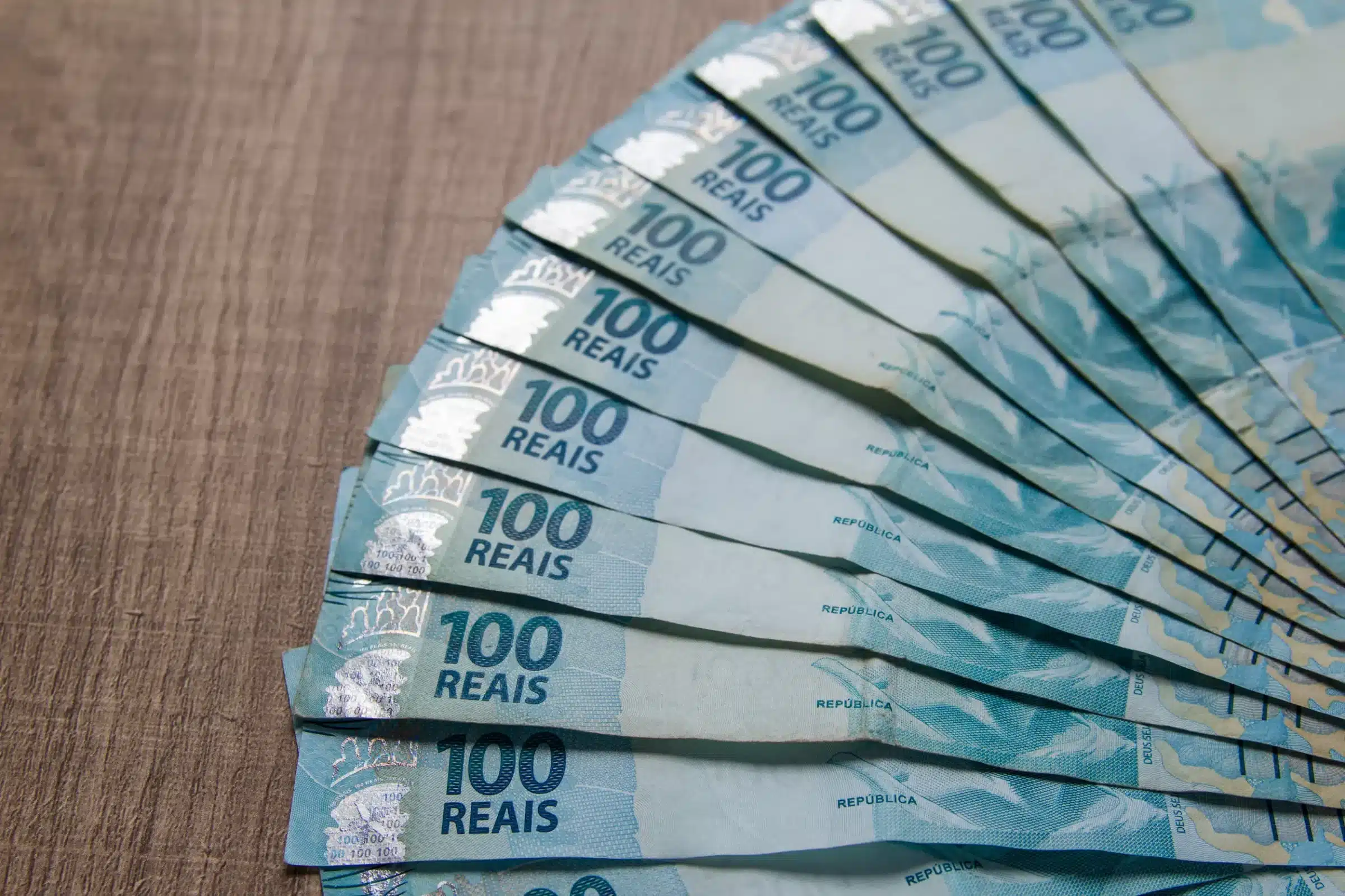 Notas de 100 reais dispostas em forma de leque, representando valores do 13º salário do INSS.