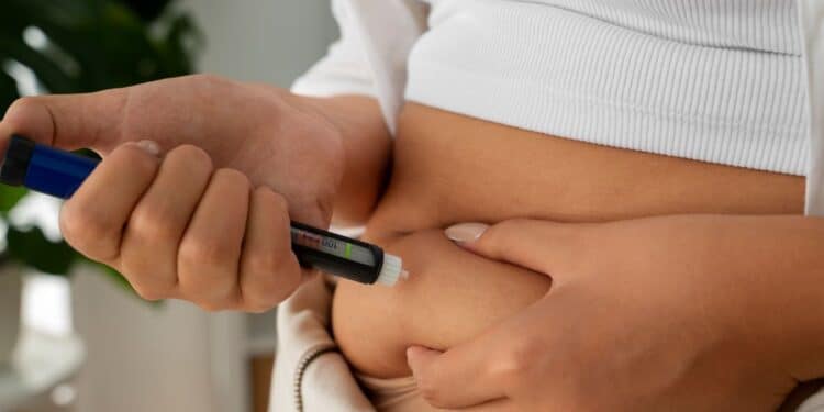 Pessoa aplicando caneta injetável de medicamento para emagrecimento na região abdominal.
