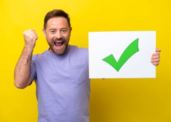 Homem celebra vitória segurando placa com sinal de aprovação verde.