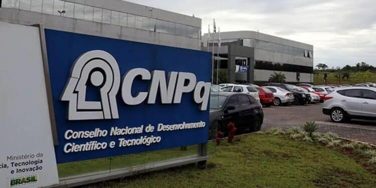 Logotipo do CNPq, localizado na sede do Conselho Nacional de Desenvolvimento Científico e Tecnológico, com fundo de carros estacionados.