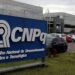 Logotipo do CNPq, localizado na sede do Conselho Nacional de Desenvolvimento Científico e Tecnológico, com fundo de carros estacionados.