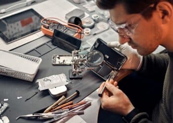 Técnico reparando celular com lupa e chave de fenda, ilustrando o aumento no conserto de celulares usados no Brasil.