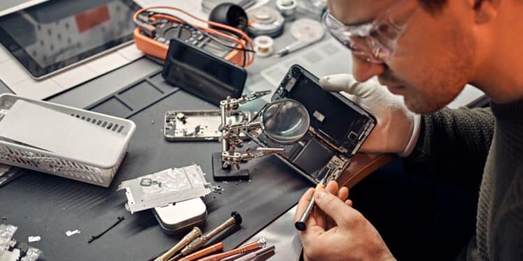 Técnico reparando celular com lupa e chave de fenda, ilustrando o aumento no conserto de celulares usados no Brasil.