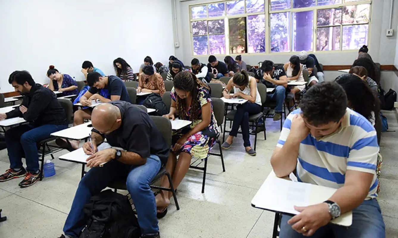 Estudantes em sala de aula realizando prova escrita em ambiente de avaliação educacional.