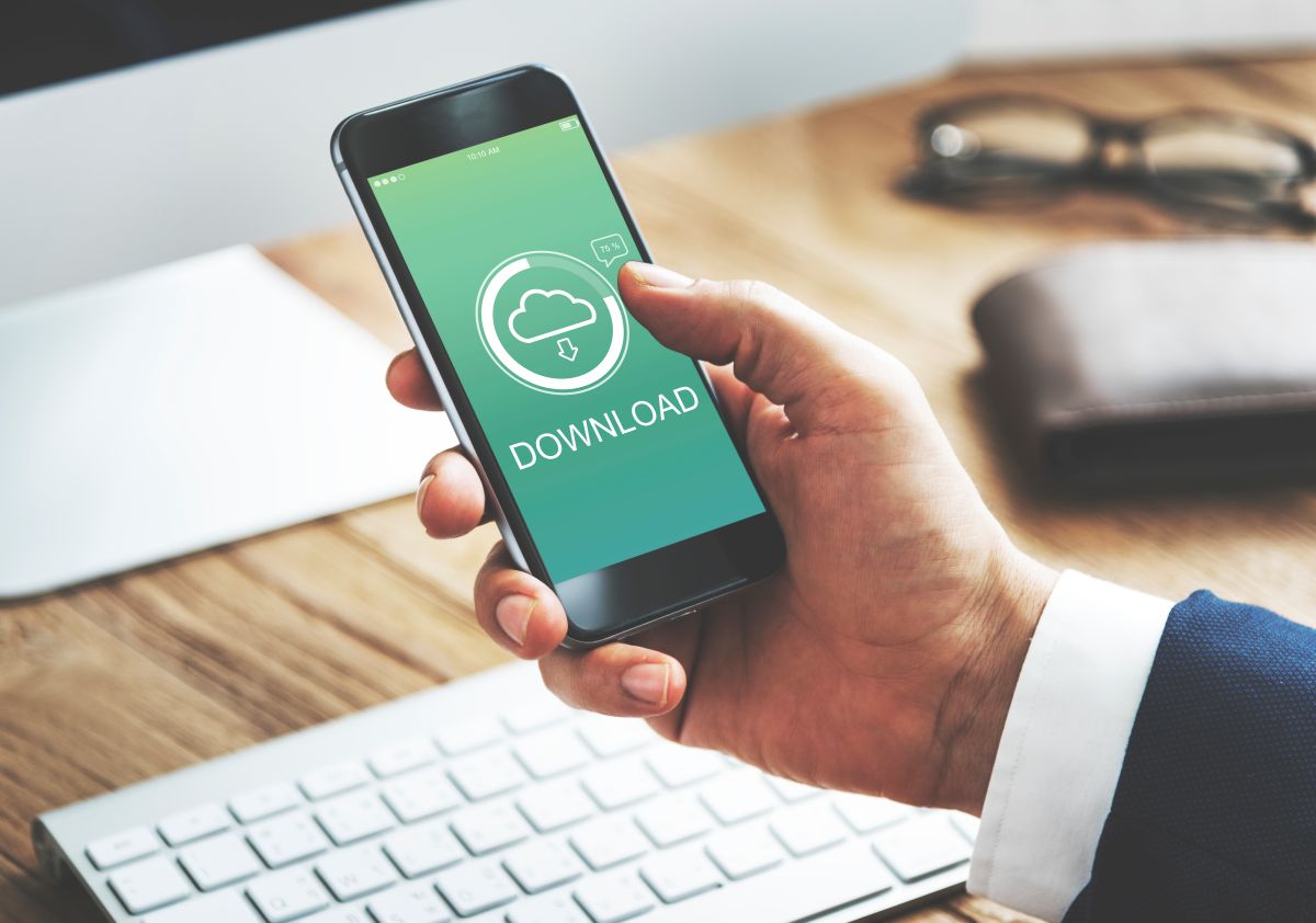 Pessoa segurando smartphone com ícone de download na tela, simbolizando a transferência de arquivos pela nuvem.
