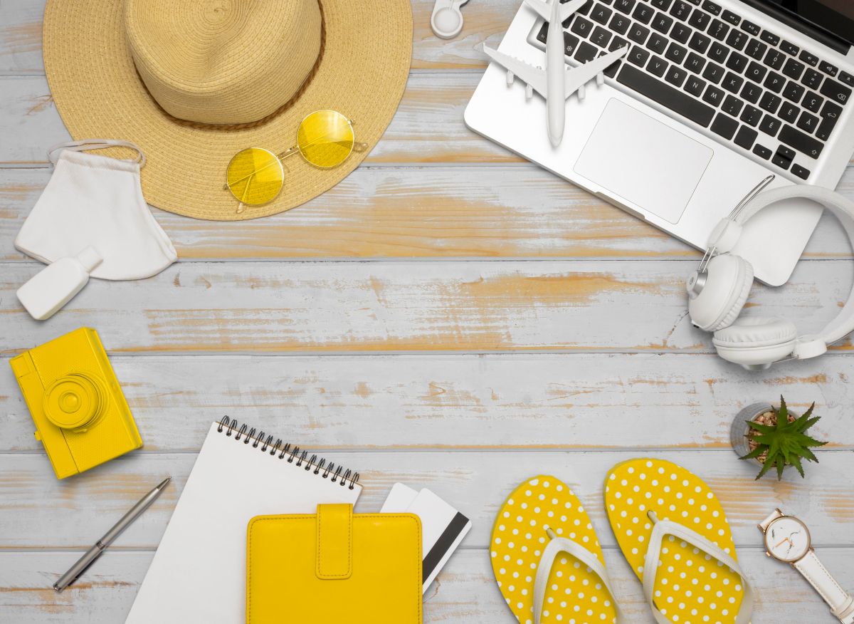 Objetos de viagem e trabalho sobre mesa, incluindo notebook, chinelos e acessórios, simbolizando descanso no feriado prolongado.