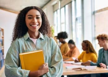 Estudante sorrindo com livros, representando o aumento da bolsa-estágio para 14 mil alunos.